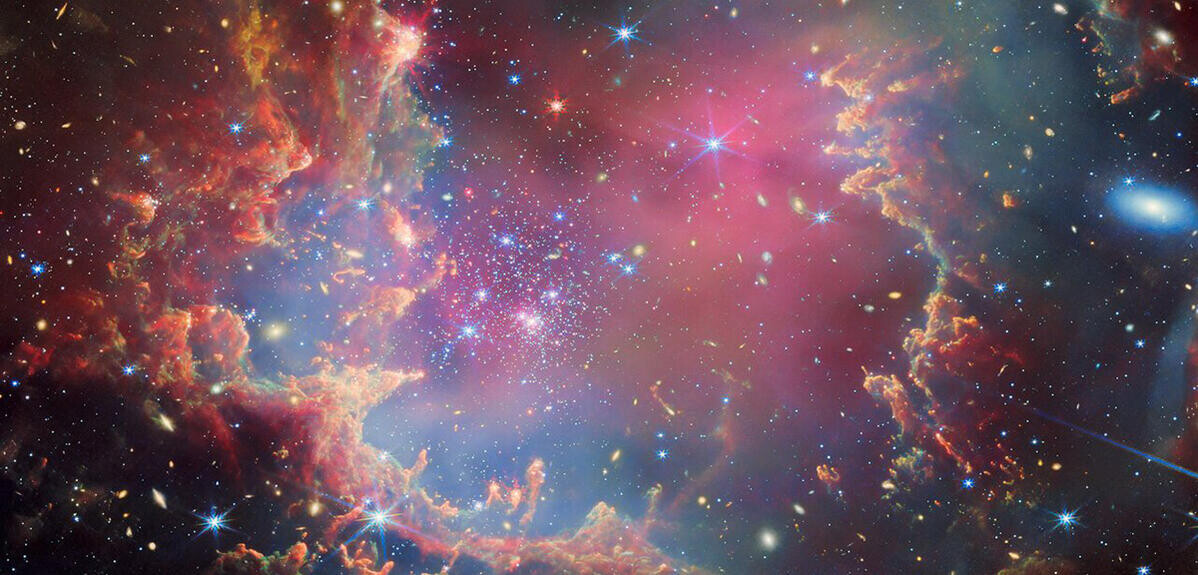 Near the outskirts of the Small Magellanic Cloud, a satellite galaxy roughly 200 000 light-years from Earth, lies the young star cluster NGC 602, which is featured in this new image from the NASA/ESA/CSA James Webb Space Telescope. This image includes data from Webb’s NIRCam (Near-InfraRed Camera) and MIRI (Mid-InfraRed Instrument). The local environment of this cluster is a close analogue of what existed in the early Universe, with very low abundances of elements heavier than hydrogen and helium. The existence of dark clouds of dense dust and the fact that the cluster is rich in ionised gas also suggest the presence of ongoing star formation processes. This cluster provides a valuable opportunity to examine star formation scenarios under dramatically different conditions from those in the solar neighbourhood. [Image description: A star cluster is shown inside a large nebula of many-coloured gas and dust. The material forms dark ridges and peaks of gas and dust surrounding the cluster, lit on the inner side, while layers of diffuse, translucent clouds blanket over them. Around and within the gas, a huge number of distant galaxies can be seen, some quite large, as well as a few stars nearer to us which are very large and bright.]